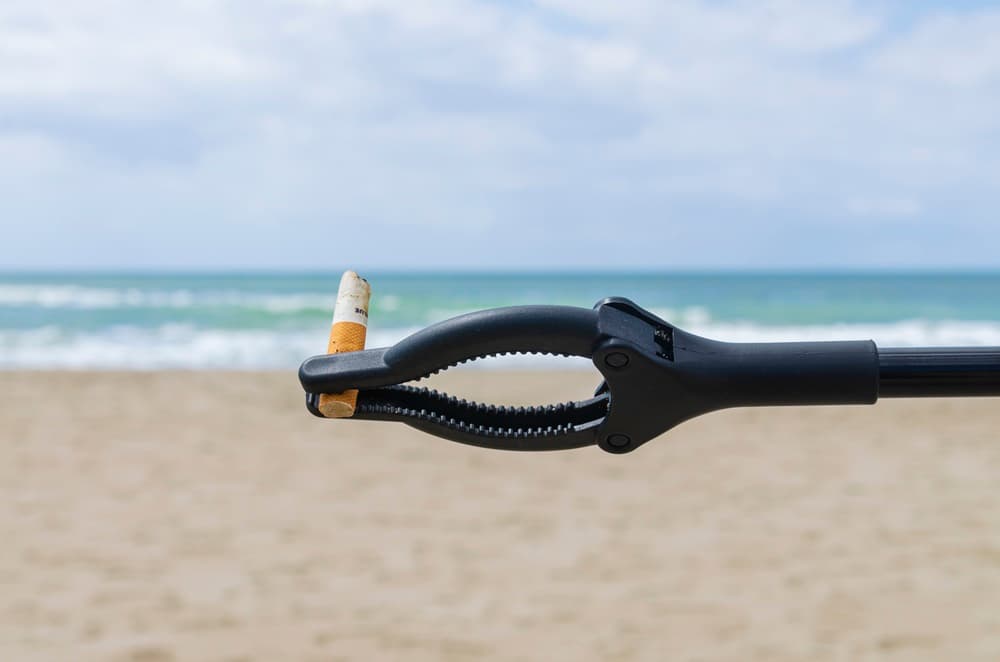 sullo sfondo di spiaggia e mare una pinza in primo piano tiene un mozzicone di sigaretta