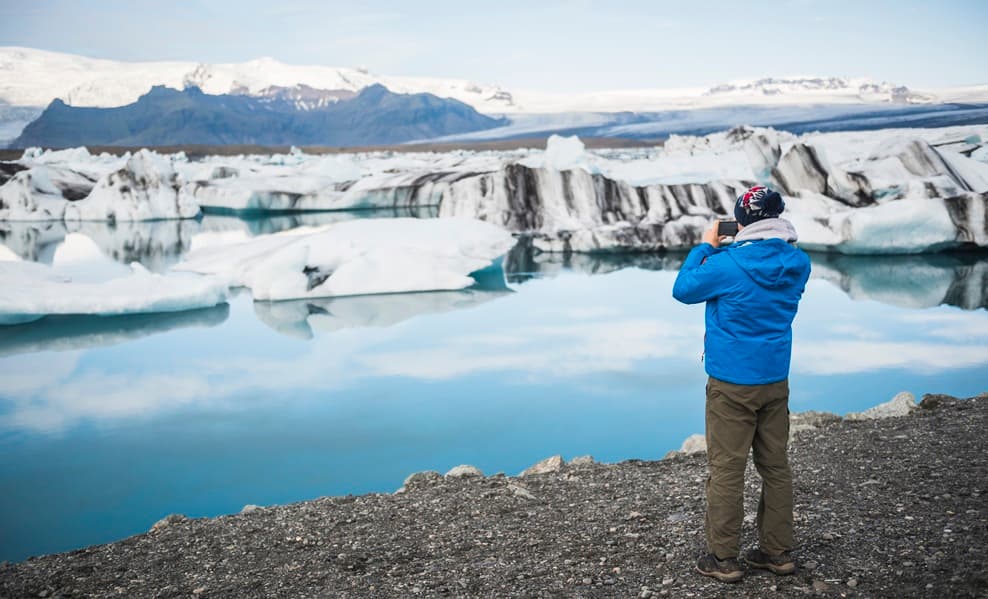 Turista fotografa lago gliacile con iceberg