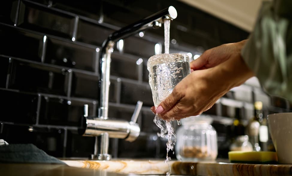 una persona, si vedono solo le mani, riempie un bicchiere di acqua dal rubinetto della cucina